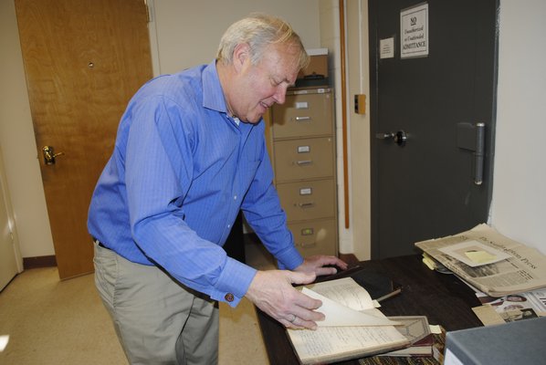 Southampton Town Historian Zach Studenroth flips through a book of handwritten Hampton Bays minutes from the early 1900s. AMANDA BERNOCCO