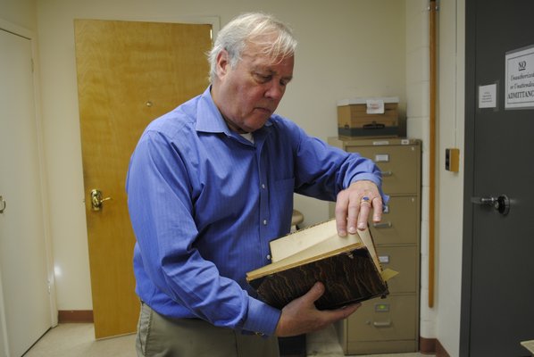 Southampton Town Historian Zach Studenroth flips through a book of handwritten Hampton Bays minutes from the early 1900s. AMANDA BERNOCCO