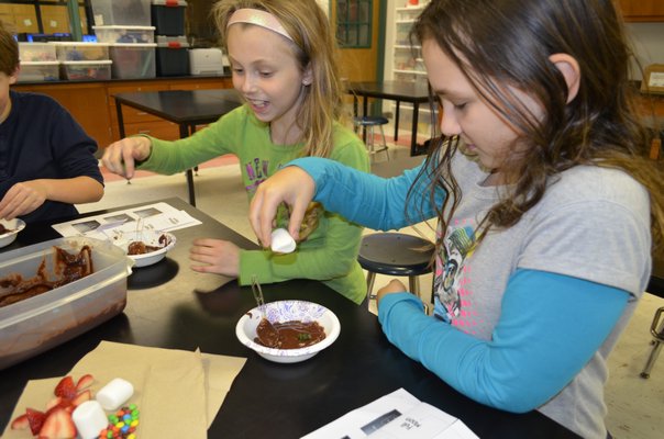 East Quogue Elementary School Astronomy Club members Jadyn Kass, left, and Carolina Pondo learned about the impacts of different substances on the moon's surface using chocolate pudding. ALEXA GORMAN