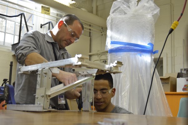Bridgehampton Robotics co-captain Claudio Figueroa works on a robot part with the help of the team's faculty advisor Ken Giosi at the Bridgehampton School on Monday. In the back, the team's robot for a competition later this month, wrapped and ready to go.