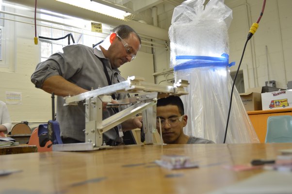 Bridgehampton Robotics co-captain Claudio Figueroa works on a robot part with the help of the team's faculty advisor Ken Giosi at the Bridgehampton School on Monday. In the back, the team's robot for a competition later this month, wrapped and ready to go.