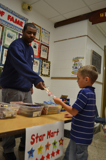 Eastport South Manor Junior-Senior High School student James McClease hands a prize to first-grade student Aidan at the Star Mart.
