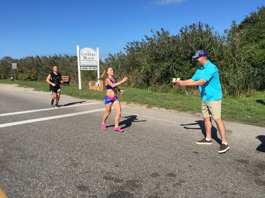 A volunteer goes to hand water to Paige Clark, who wound up finishing third overall among women in the marathon. MICHELLE MALONE