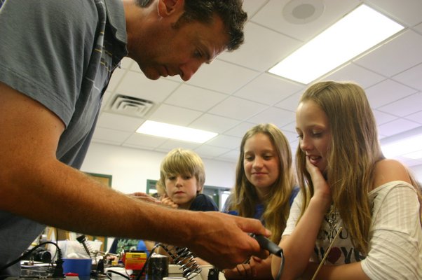 From left, Brad Murphree teaches Jack Romano, 11, Mary Koltzan, 9, and Gabrielle Johnson, 10, (all East Quogue residents) how to solder the control panel for an underwater remote operated vehicle Tuesday afternoon. Murphree instructed a class of more than 30 4th and 5th graders on how to assemble the vehicles as part of a summer ocean explorer's class at East Quogue Elementary School, 6 Central Ave., East Quogue. KYLE CAMPBELL