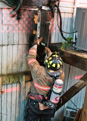 Westhampton Beach probationary firefighter Sal DiBenedetto rips away some siding during overhaul. COURTESY WESTHAMPTON BEACH FIRE DEPARTMENT