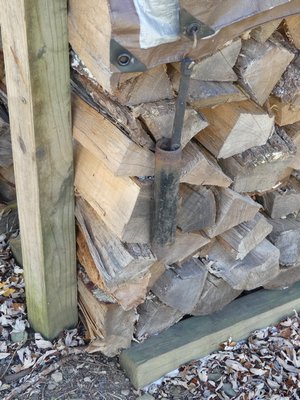 The end of this outdoor firewood stack is supported by a pressure-treated 4-by-4 (vertical on the left) and the wood stacked atop horizontal 4-by-4s to keep the wood off the ground. Note the piece of cast iron pipe attached to the eyelet in the tarp using a bungee cord. Later in December the tarp will be unfolded for better winter protection but the tarp and pipe weights should never reach the ground, where they can freeze solid and make the firewood inaccessible. ANDREW MESSINGER