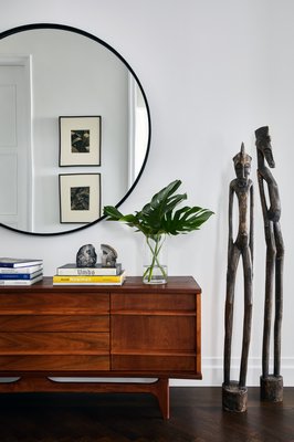 In a newly constructed home's foyer, a mid-century credenza is enjoyed while a set of African statutes is admired. CHRISTIAN HARDER