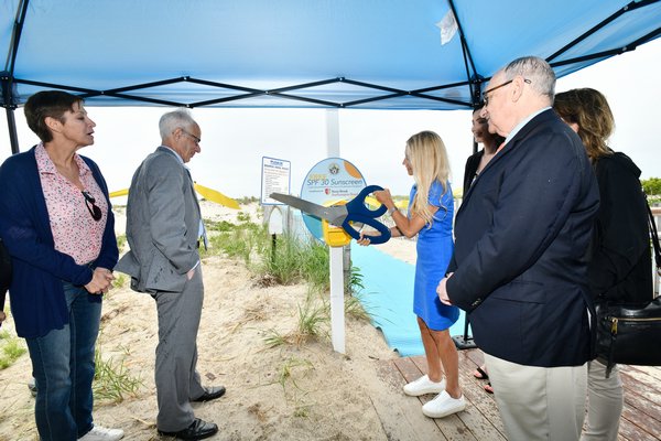Southampton Town Councilwoman Christine Scalera cuts the ribbon at the sunscreen station at Ponquogue Beach in Hampton Bays on Tuesday morning.  DANA SHAW