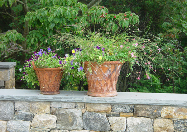 Two whimsical pots standing alone on a capped stone wall, breaking the otherwise structured and linear form of the wall.