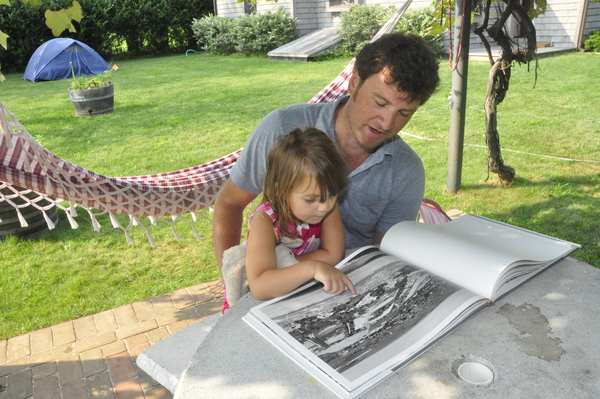 Zak Powers flips through his photo book, "Further Lane," with his three-year-old daughter, Lyla, in Amagansett last week. MICHELLE TRAURING