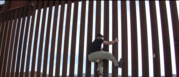 Dennis Michael Lynch grabs ahold of the fence separating Mexico from Arizona. COURTESY DENNIS MICHAEL LYNCH