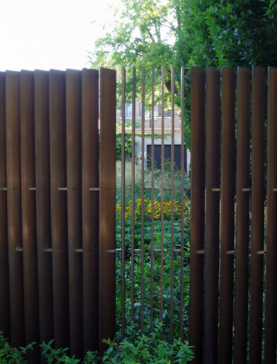 Creative bronze fence made of slats turned at an angle allows a view into the garden.