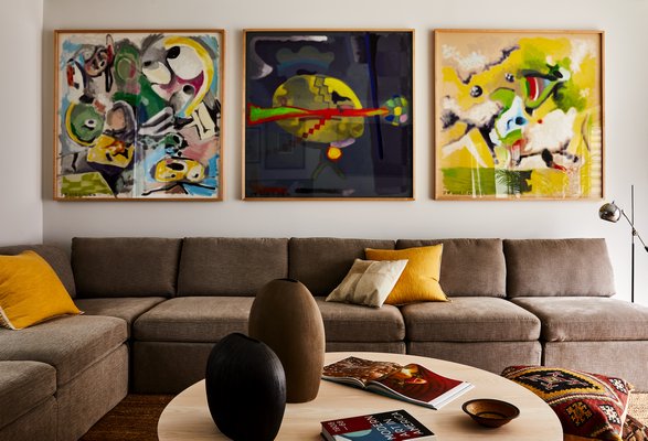 A trio of paintings by Jeffrey Alan Scudder (courtesy of Creative Art Partners) hangs in an East Hampton family room. Note how the primary colors of yellow, red, and blue in the art are echoed in the accessories and pillows below. CHRISTIAN HARDER