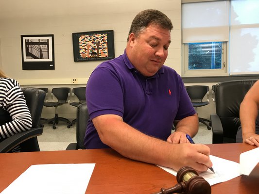 J.P. Foster, preisdent of the East Hampton School District Board of Education, signing a contract at Tuesday's school board meeting for the district to purchase a property on Springs-Fireplace Road to build a bus depot. JON WINKLER