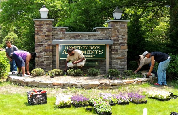 Hampton Bays Apartments tenants, staff and YouthBuild members tend to plants surrounding the front sign. YOUTHBUILD