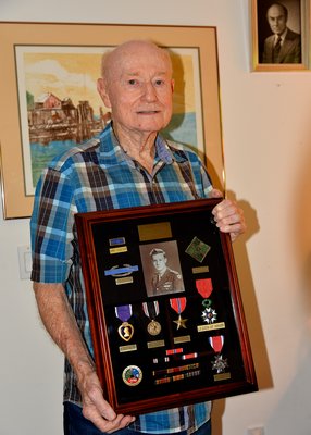 Martin Sylvester at his home in Springs, holding his war awards. 
Medals: Purple Heart, Prisoner of War, Bronze Star, Legion of Honor, N.Y.S. Distinguished Service Medal.      
Ribbons: WWII Victory, Good Conduct, European Theater, Three Battle Stars. 
Other: Unit Citation, Combat Infantry Badge, Ivy Leaf Patch (4th Infantry)