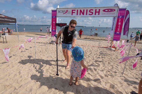 Matthew Plourde accepts a bottle of water from 2-1/2-year-old Mia Pardo as he crosses the finish line during the annual Paddle for Pink at Havens Beach on Saturday morning.