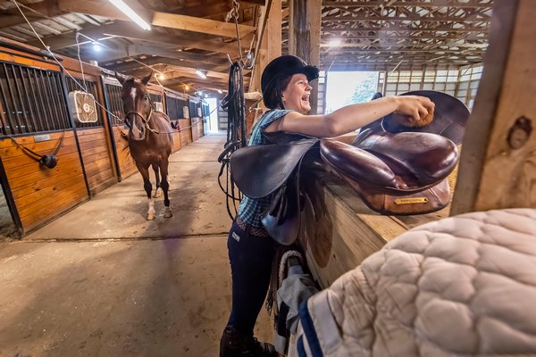 Phobe Topping laughs with a friend as she cleans a saddle inside the stable.
