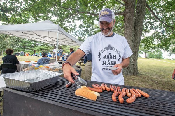 Park Board President Gregg Schiavoni cooks up some dogs on the grill during the Mash at Bash fundraiser event to commemorate the anniversary of Woodstock at Mashashimuet Park on Sunday afternoon.   MICHAEL HELLER