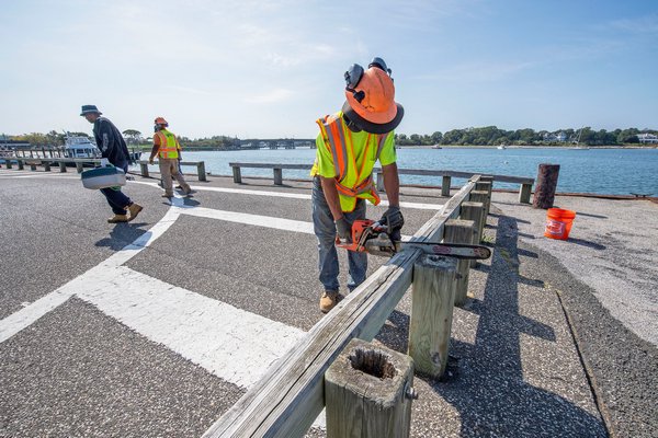 As the last fisherman to fish off the old wharf leaves, at left, work begins to remove the old wooden guardrails during the project to renovate Long Wharf in Sag Harbor on Monday.  MICHAEL HELLER