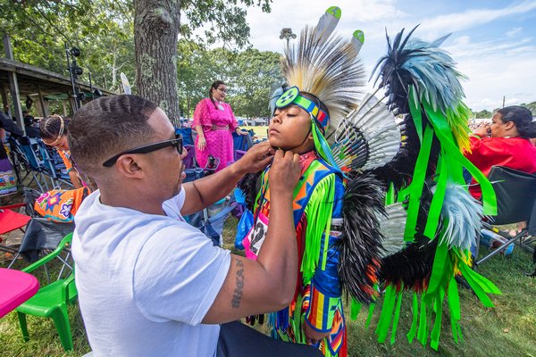 Micah Hunter helps his son Koda with his regalia prior to the start of the Grand Entry parade during the 2019 Shinnecock Powwow on Sunday.