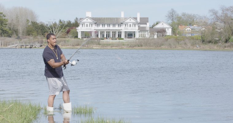Shane Weeks, a member of the Shinnecock Indian Nation, fishes on the reservation in Southampton across from luxury homes.
