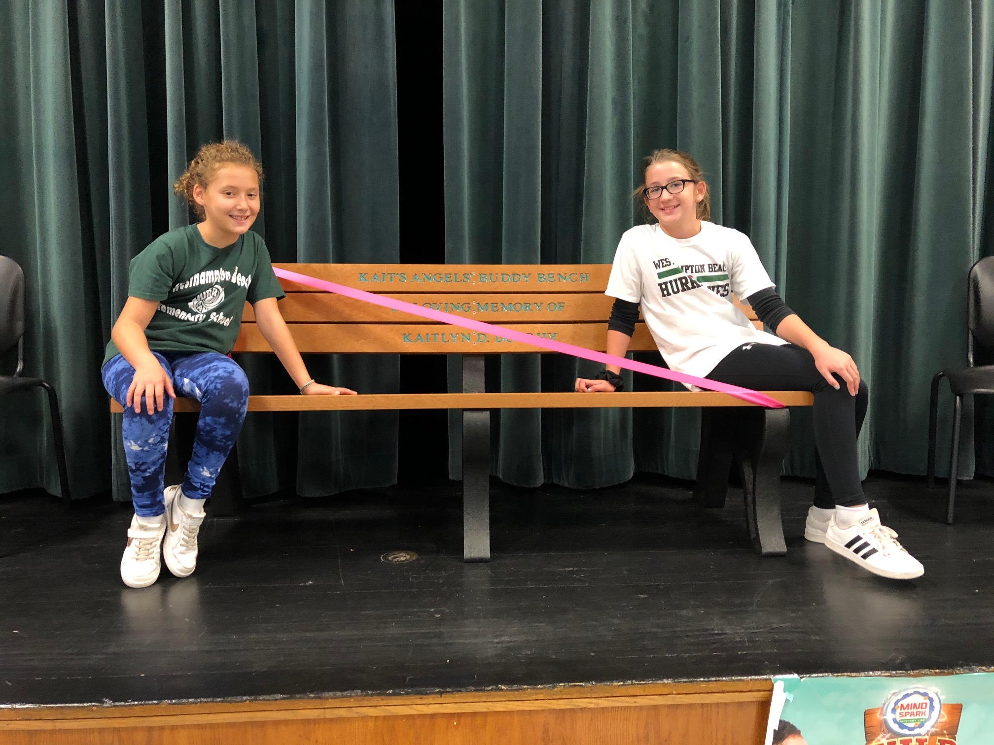 Westhampton Beach Elementary School students Elizabeth Sultan and Amanda Michne sit on the new Kait's Angels buddy bench, donated by the benevolent associations of Westhampton Beach Village Police ande Southampton Town Police. The weather moved the presentation inside and the bench will be installed near the school's playground. The bench is the most recent donation made possible through the efforts of Kait's Angels, a group of friends of Kait Doorhy, a graduate of Mattituck High School, who was killed in 2014 after being hit by a car during her sophomore year of college. Kait's Angels aim to have a Buddy Bench at every elementary school on the North and South forks; so far every school on the North Fork has one and several schools on the South Fork.