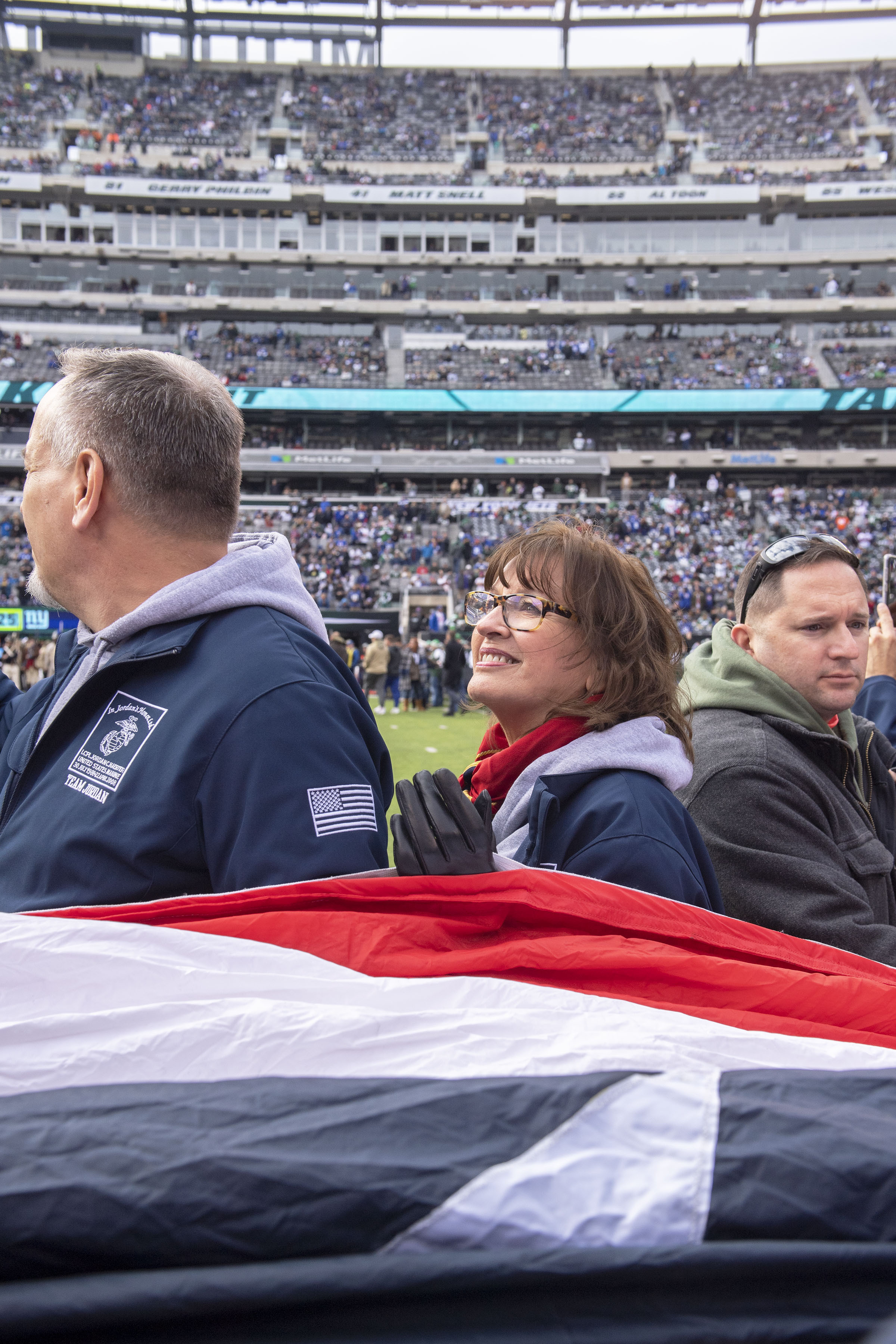 Sag Harbor Gold Star Mother JoAnn Lyles, center, accompanied by her brother Ken and several hundred Gold- and Blue-Star Families, marvels at being inside the stadium for the first time with giant American flag that was presented as part of a pre-game 