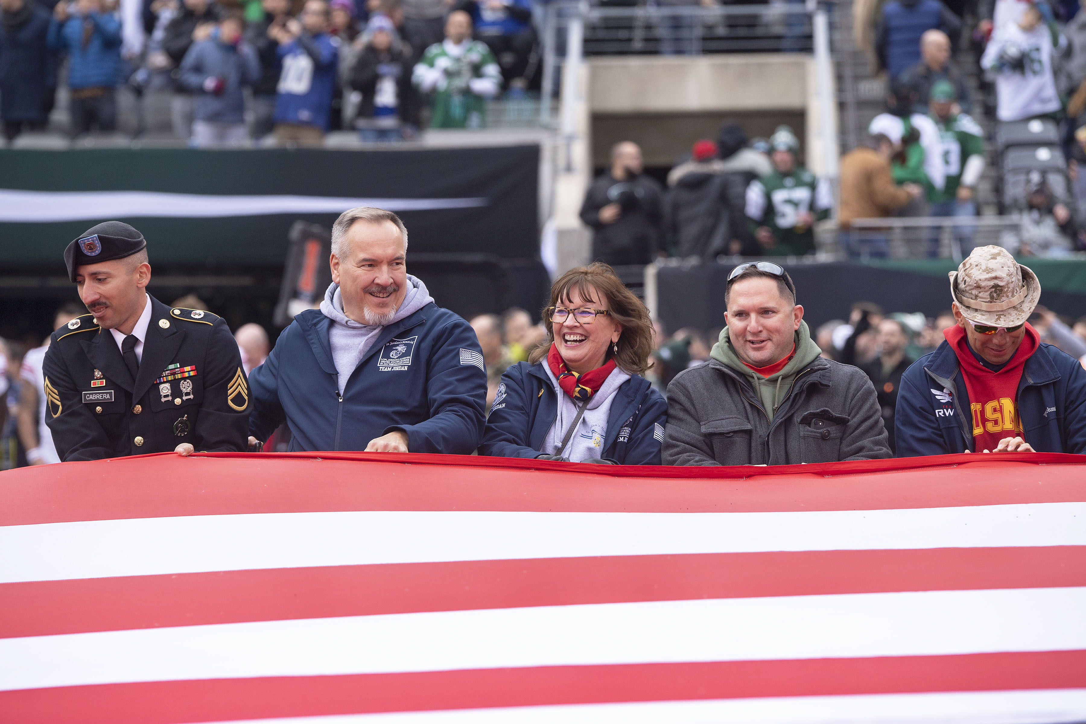 Sag Harbor Gold Star Mother JoAnn Lyles,  center, accompanied by her brother Ken, left, and several hundred Gold- and Blue-Star Families, reacts as she helps to hold open a giant American flag that was presented as part of a pre-game 