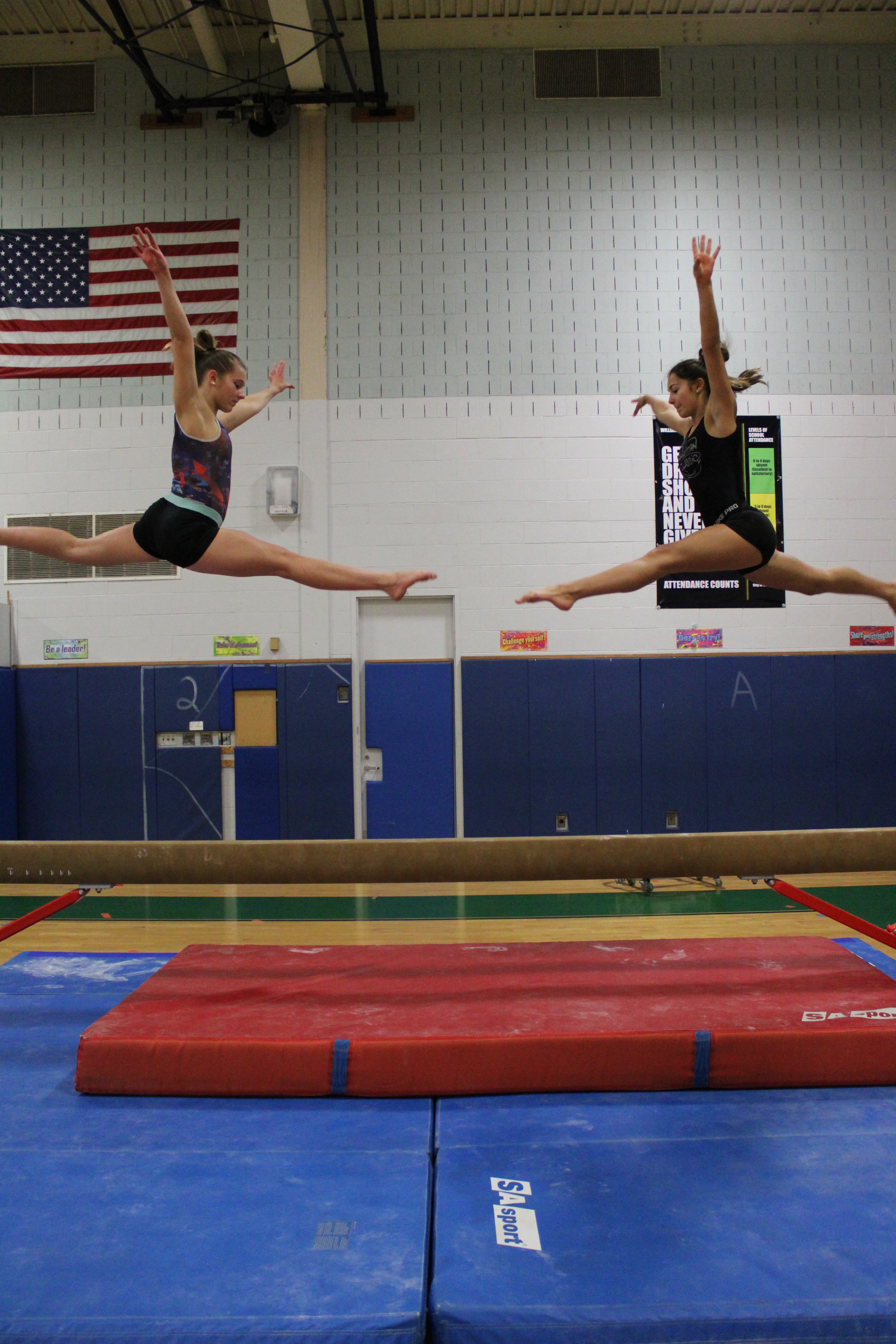 Caitlin Thrash and Taylor Bodanza both do a split jump on the blance beam. 
