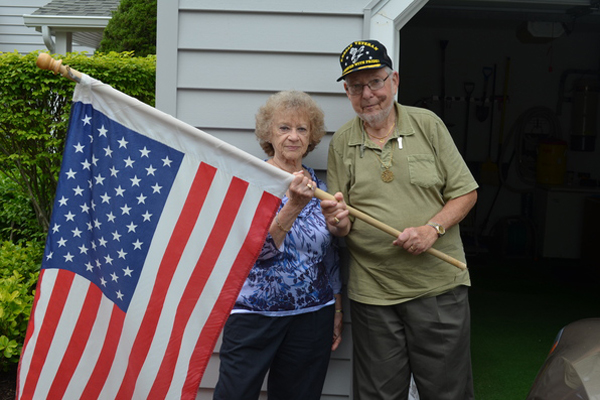 Lenore and Buddy Savetz outside of their Westhampton home holding their flag. ERIN MCKINLEY