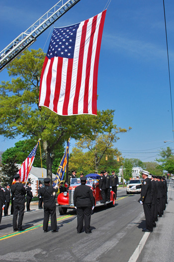 Firefighters pay tribute to Benjamin W. Lupia as his funeral procession passes the Hampton Bays firehouse on Saturday afternoon.  <br>Photo by Will James