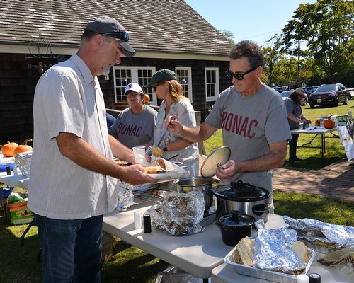 The East Hampton Historical Farm Museum hosted a community dinner on a beautiful Sunday afternoon. Peter Van Scoyov gets a generous helping of food from Sean Bennett.  KYRIL BROMLEY