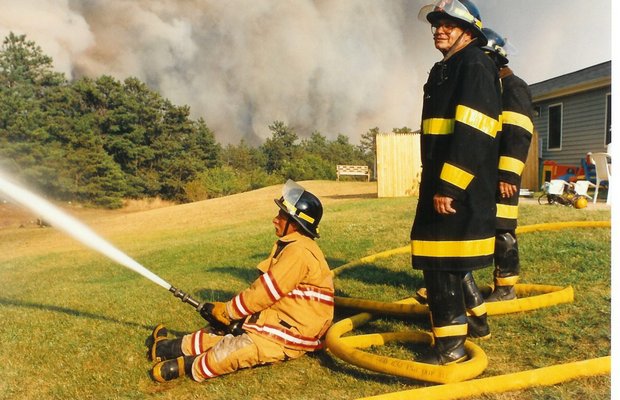 Westhampton Beach firefighter Ken Pearson douses brush fire flames during the 1995 Sunrise Wildfires while then-chief Fred Overton stands behind him COURTESY FRED BAUER