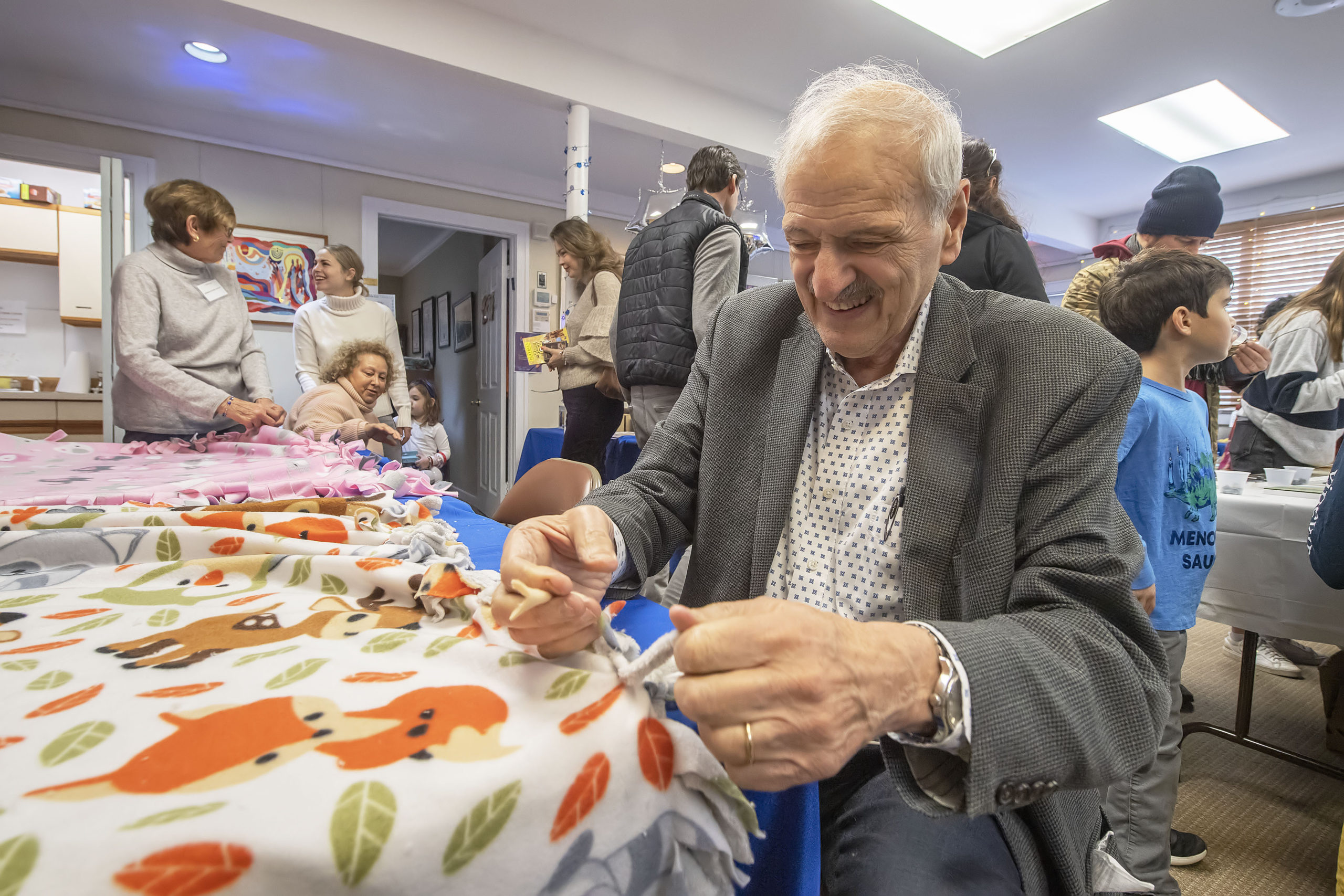 Jim Kyprios ties knots on the edges of a blanket that will be donated to children in The Retreat during the annual Hanukkah Party at Temple Adas Israel on Sunday.   MICHAEL HELLER