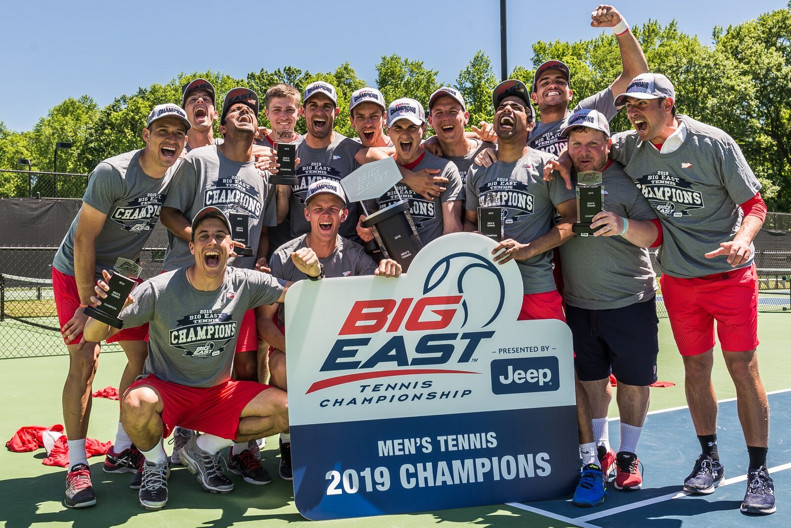 Dillon Pottish, standing directly behind the Big East sign with the Big East Championship trophy, along with Richard Sipala, standing to Pottish's right, helped lead the St. John's men's tennis team this past season as head and assistant coaches.