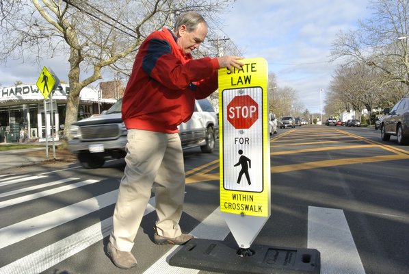 Dick Bruce places a pedestrian crossing sign near Thayer's Harware in Bridgehampton on Thursday afternoon. He also placed one in the crosswalk at the Bridgehampton Post Office.  DANA SHAW