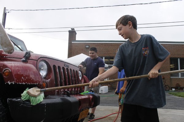 Eastport Junior Firefigher Liam McGeneva scrubs down the front end of a Jeep during the junior firefighters' car wash fundraiser Sunday morning on Union Avenue. KYLE CAMPBELL
