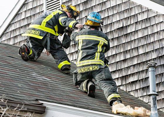 Quogue Fire Department Lieutenant Todd Bandrowski (right) hands a chain saw to firefighter Tyler Davonski in preparation for opening a vent in the roof during a joing drill between the Quogue and Westhampton Beach fire departments. COURTESY WESTHAMPTON BEACH FIRE DEPARTMENT