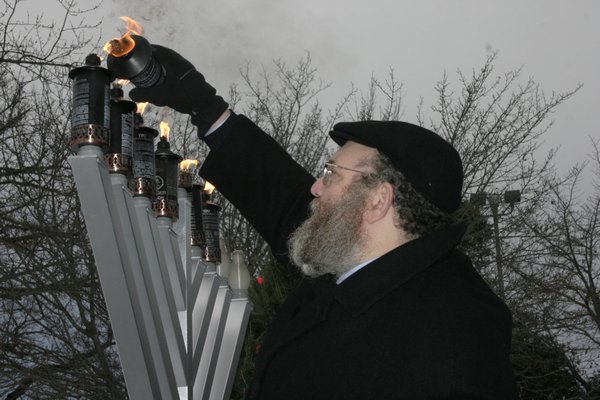 Rabbi Leibel Baumgarten of the Chabad Lubavitch of the Hamptons lights the menorah candles in Herrick Park on Sunday. MICHAEL WRIGHT