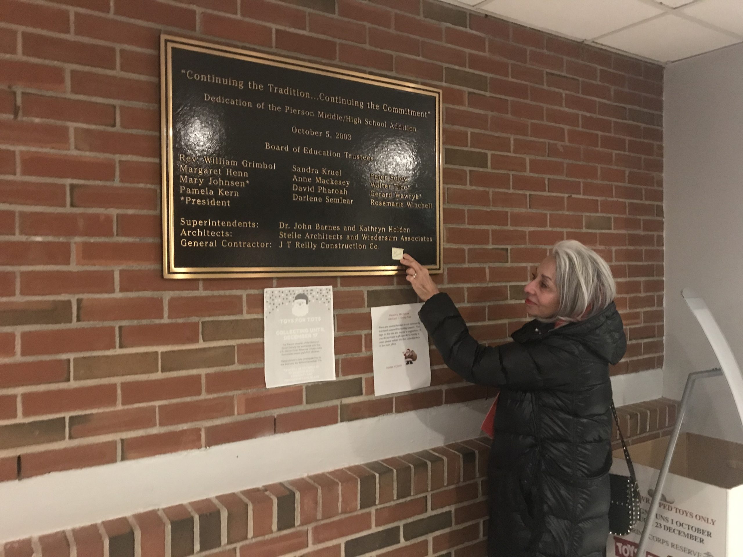 Marian Cassata places a yellow Post-It note on the plaque at Pierson Middle-High School commemorating the school's expansion in 2003. Board members agreed to add her husband's name, former principal Robert Schneider, to the plaque to honor is efforts to make the expansion a success. 