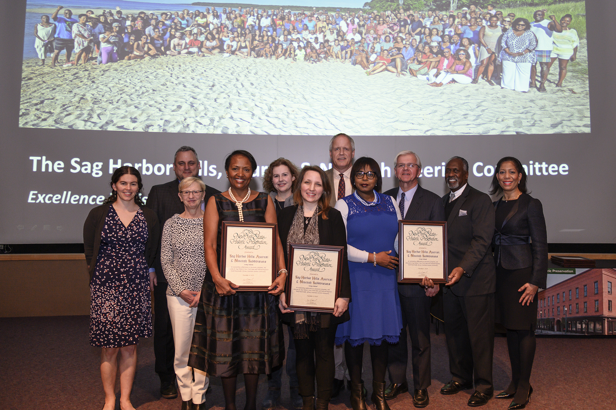 Members of the Sag Harbor Hills, Azurest and Ninevah (SANS) steering committee were honored at the New York State Preservation Awards at the Huxley Auditorium at the New York State Museum in Albany last month. Among those in the photo are, from left to right with plaques, SANS president Renee Simons, Sarah Kautz of Preservation Long Island, and Georgette Grier-Key, the director of the Eastville Community Historical Society. Other guests included, from left to right, Assemblyman Fred W. Thiele Jr., Eglon Simons, the past Sag Harbor Hills president, and attorney Lisa Stenson Desamours. The group, which was joined by representatives of state's Office of Parks and Historic Preservation, is standing in front of a photo of the 2019 Labor Day weekend gathering of SANS residents taken by John Pinderhughes. 