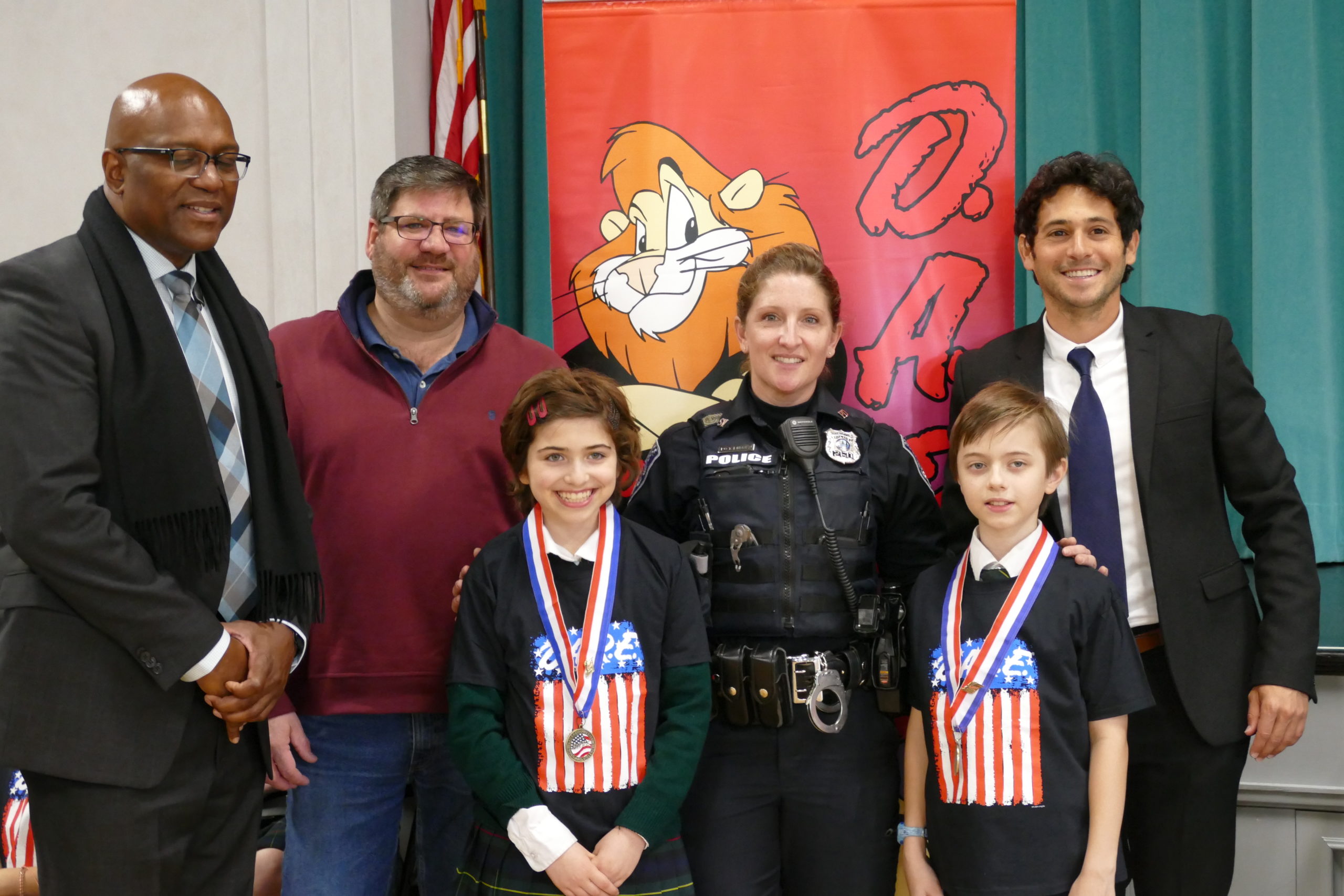 Southampton Police Officer Tiffany Lubold presented Our Lady of the Hamptons School fifth-graders with certificates of completion at the DARE graduation on January 10. Also attending the ceremony were Southampton Village Mayor Jesse Warren, right,  Southampton Village Police Detective Herman Lamison, left, and Southampton Village Trustee Richard Yastrzemski. Essay contest winners Lucy Tillotson and Oliver Nielsen read their essays on the lessons learned in the program.