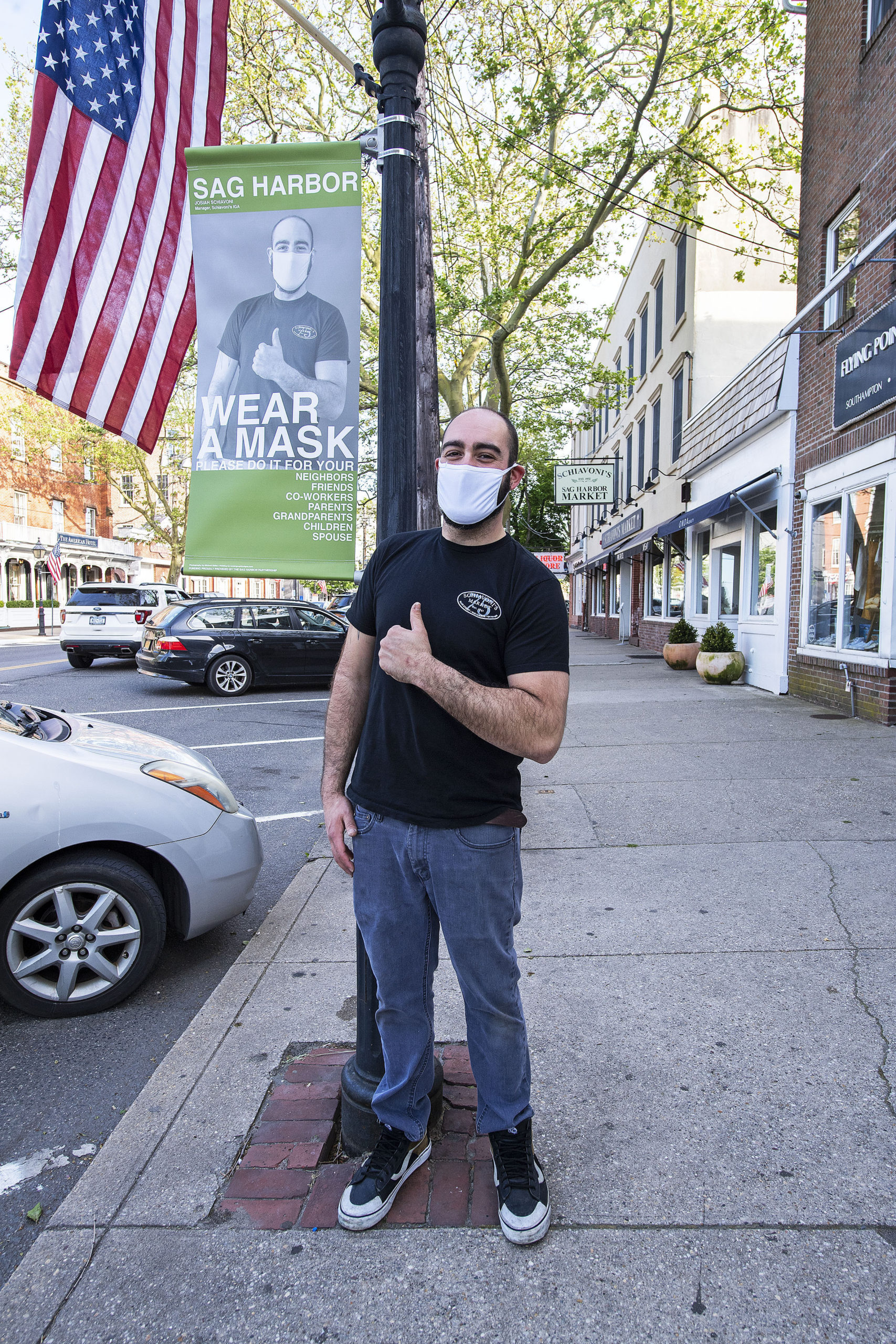 Josiah Schiavoni in front of the banner on Main Street he posed for as part of the Sag Harbor Wear A Mask campaign, photographed on Friday.  MICHAEL HELLER