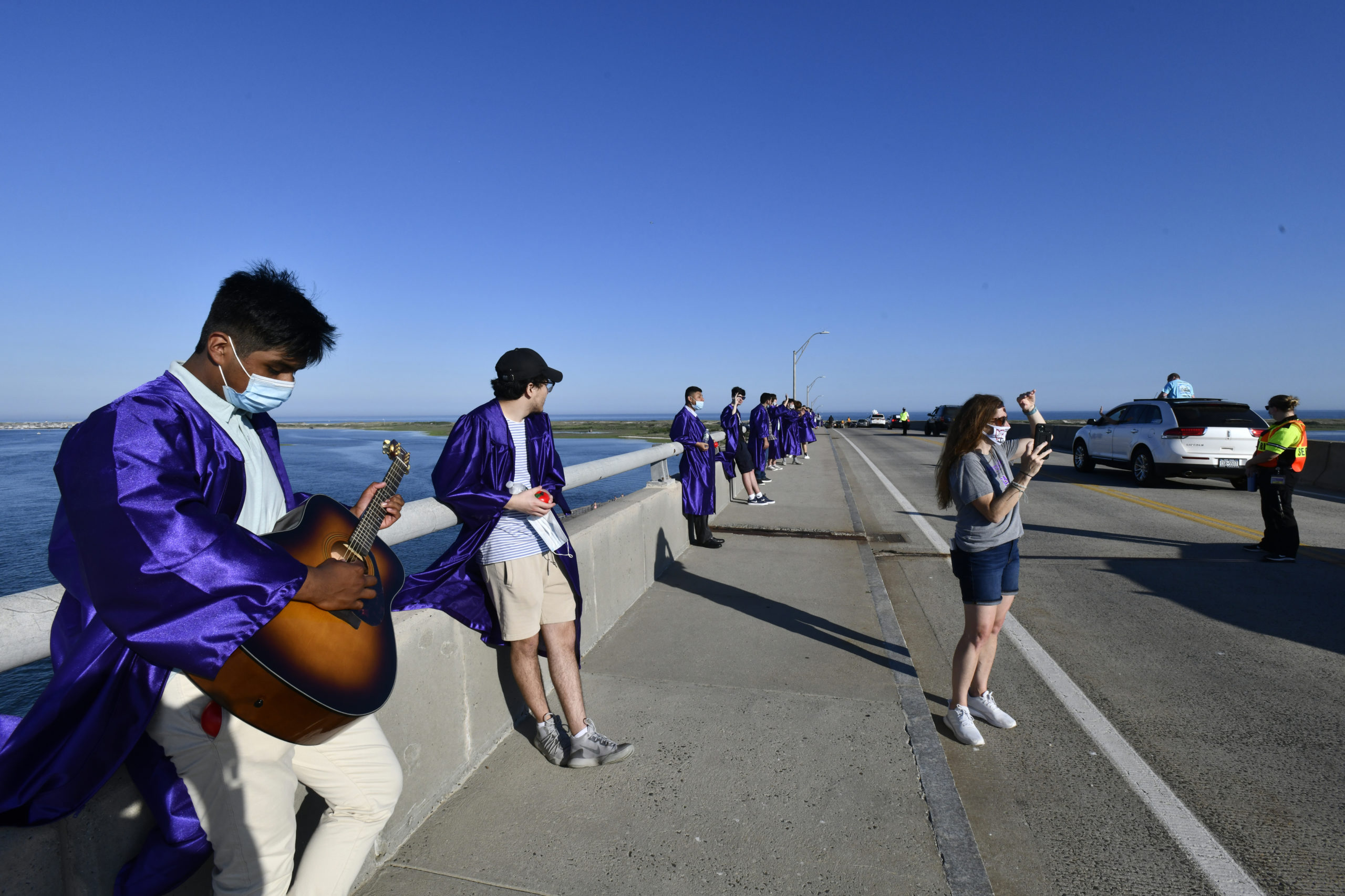 Hampton Bays graduate Gabriel Rojas strums a guitar on the Ponquogue Bridge on Monday evening as friends and family drive by to congratulate the graduating class. DANA SHAW