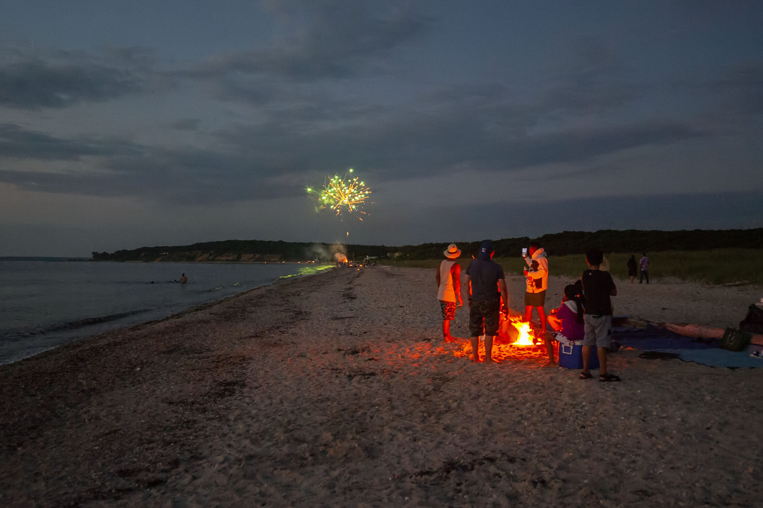 A family watches from around their campfire as another party sets off their own fireworks on the beach as part of a July 4th celebration as the sun goes down at Maidstone Park Beach on Saturday evening.    MICHAEL HELLER