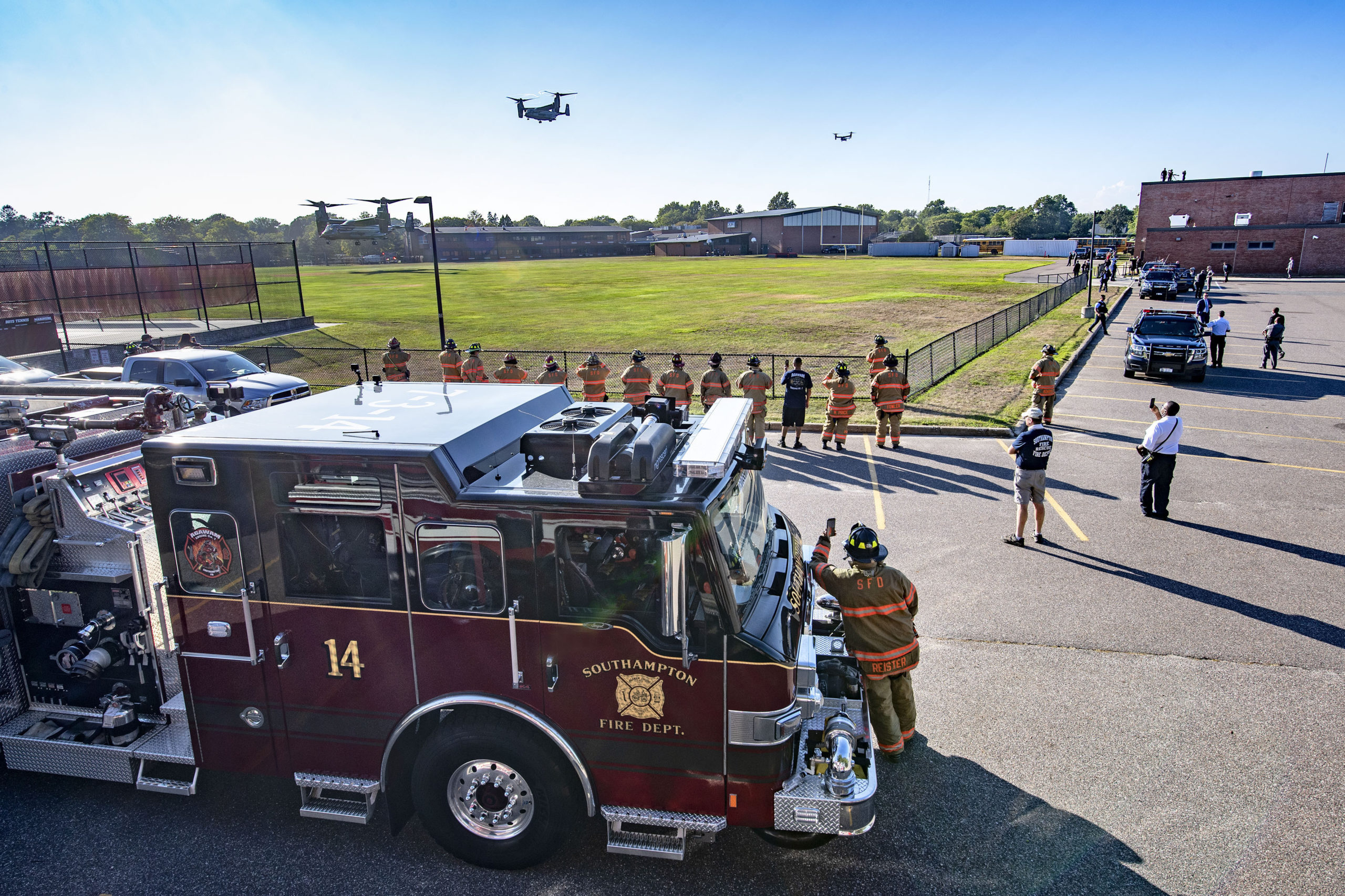 Members of the Southampton Fire Department look on as Marine Osprey aircraft carrying presidential staff come in for a landing at the athletic fields behind Southampton High School during President Trump's visit to the Hamptons on Saturday.    MICHAEL HELLER
