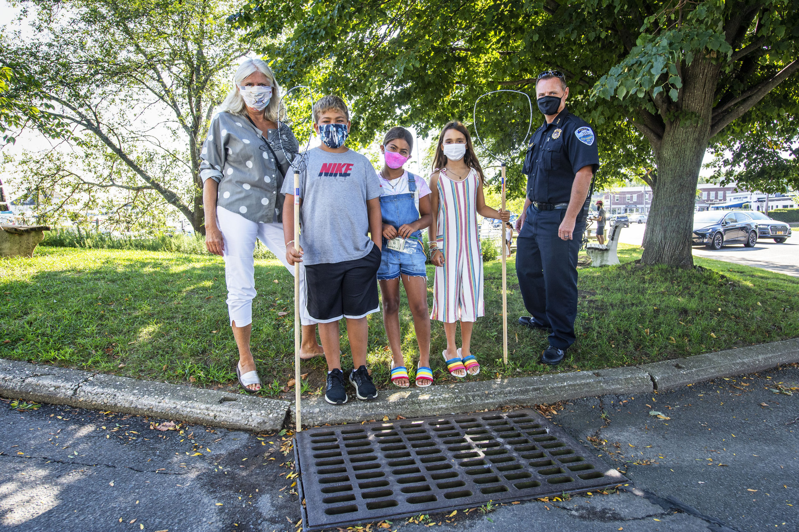 Kyle and Elle Maslin, along with their friend Lila Wiesenthal, pose for a photo with Sag Habor Village Mayor Kathleen Mulcahy and Police Chief Austin McGuire at the storm drain at the corner of Marine Park and Bay Street where the kids, with help from Chief McGuire, rescued a young duckling that was caught in the drain. MICHAEL HELLER