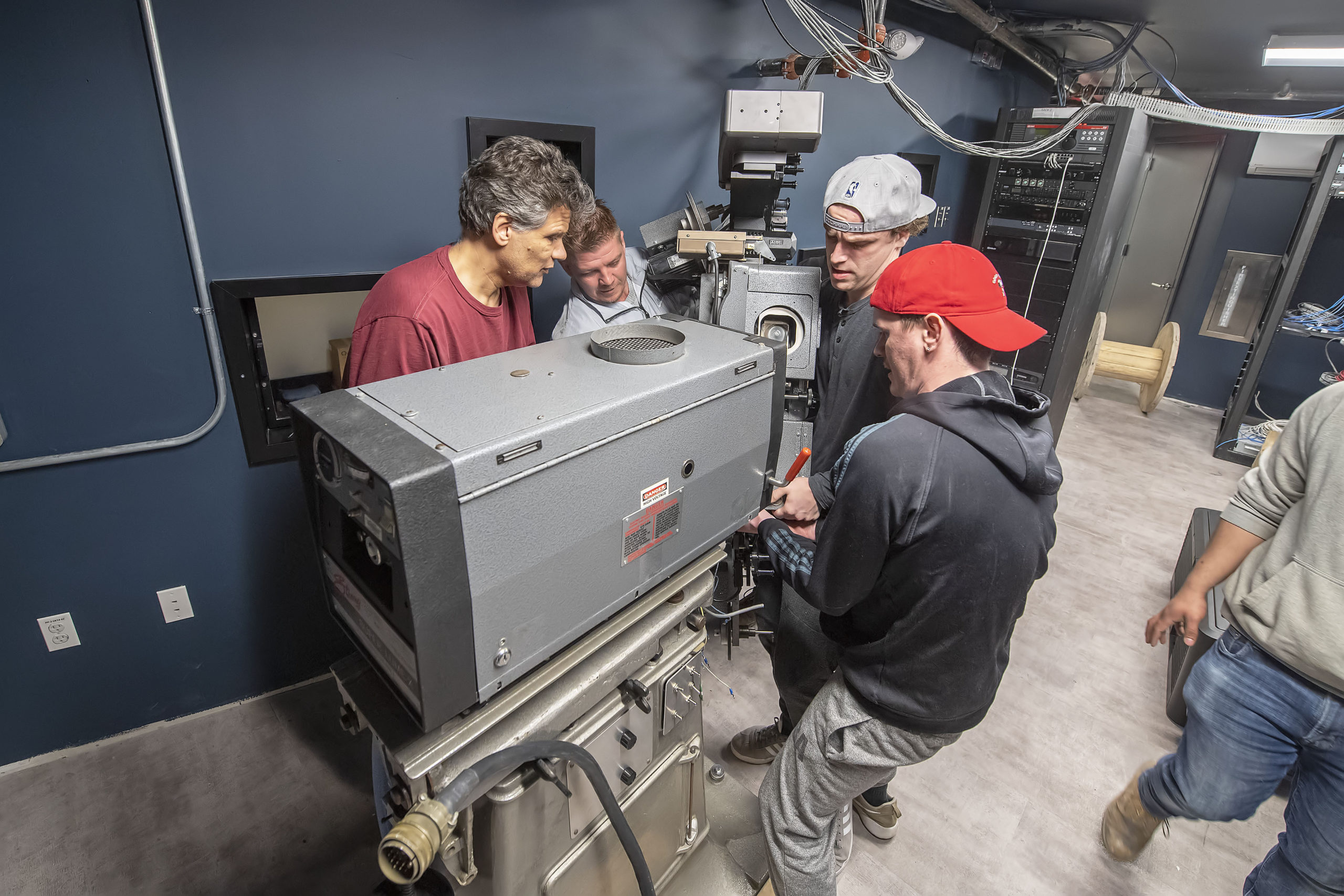A 200, plus, pound top section of a 35mm projector is muscled into position by a team of four men in its new home in the projection room of the new Sag Harbor Cinema in March.  MICHAEL HELLER