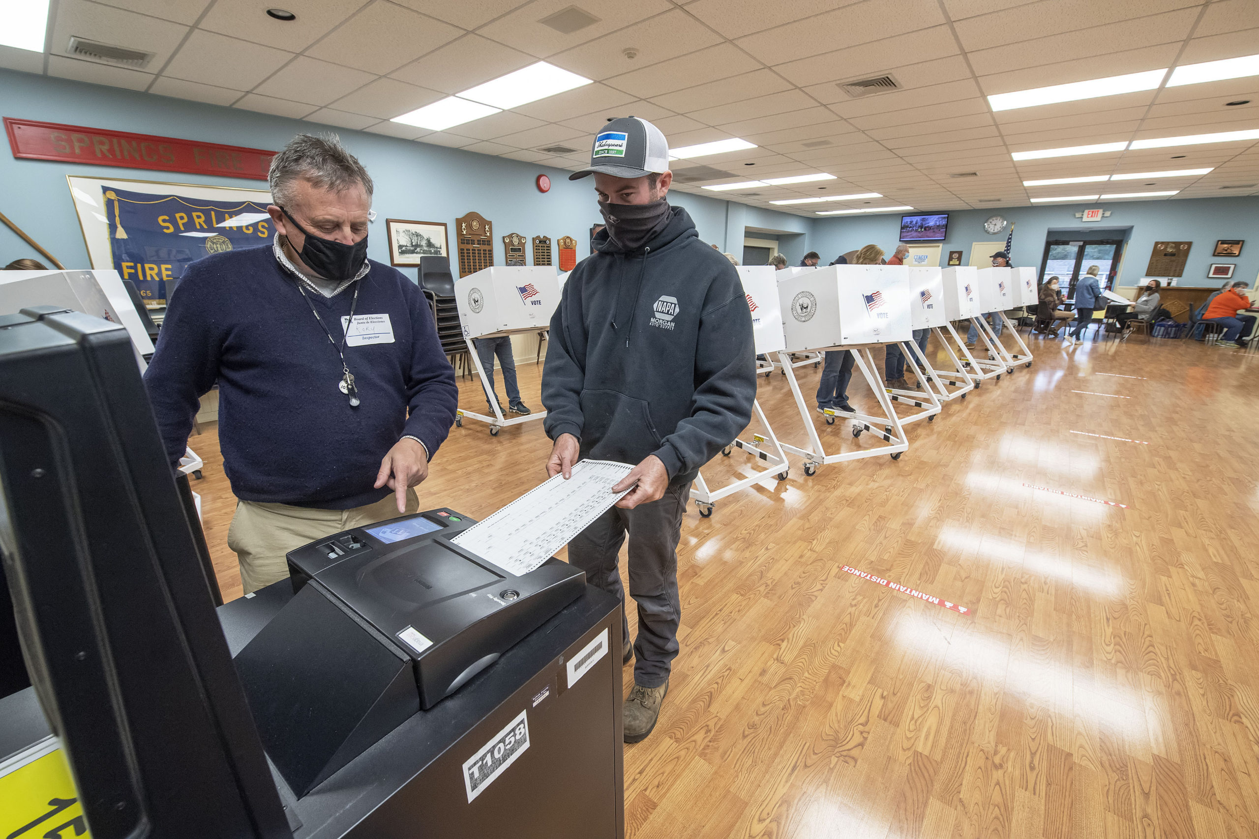 Poll Worker Rory Conway helps a voter feed his ballot into a voting machine at the polling station at the Springs firehouse on Election Day morning.   MICHAEL HELLER